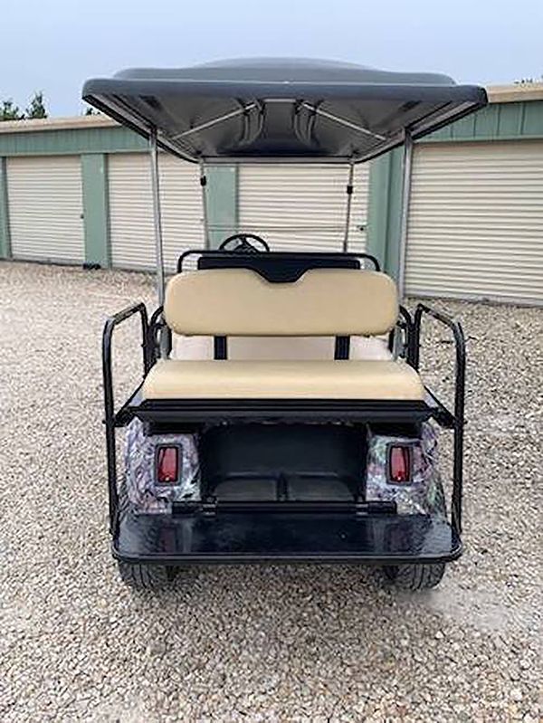 Rear view of a beige golf cart with black canopy parked on gravel in front of storage unit doors