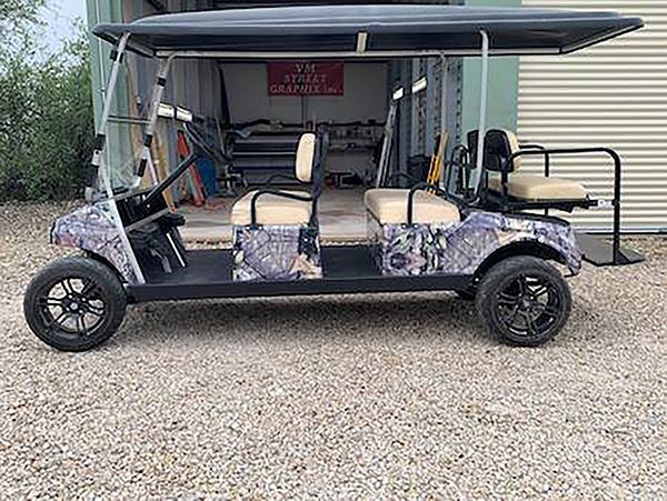 Black golf cart with beige seats and a canopy parked on gravel outdoors