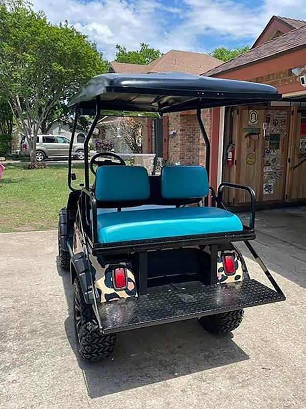 Blue golf cart parked outdoors beside a building and trees