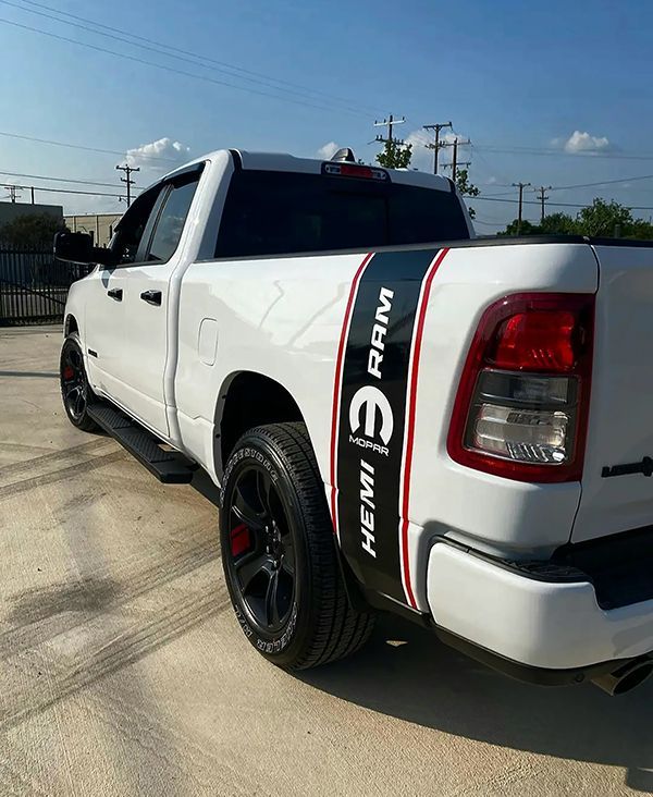 White pickup truck with black rims and red stripe decals parked outdoors in sunlight