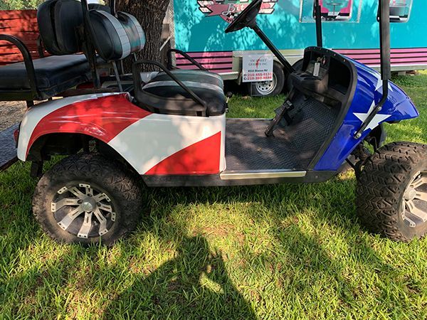 Red, white, and blue off-road golf cart parked on grass under a canopy.