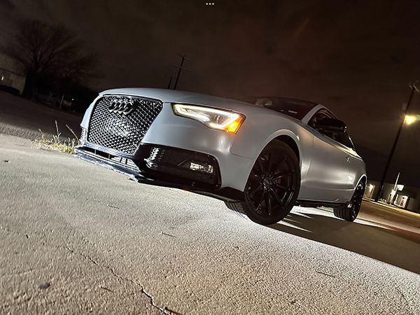 Silver Audi coupe parked at night on a street, viewed from a low angle.