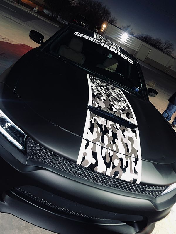 Black car with a white camouflage hood stripe parked at dusk.