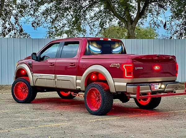 Maroon and beige lifted Ford pickup with red rims, parked on pavement under trees