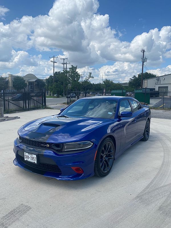 Blue sports sedan parked on a concrete lot under a cloudy sky