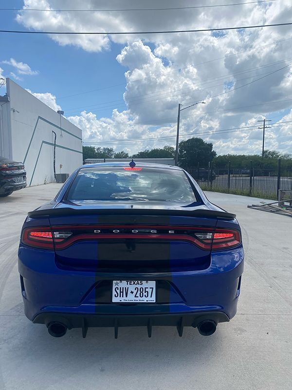 Blue Dodge Charger parked outdoors under a cloudy sky, rear view with visible license plate.
