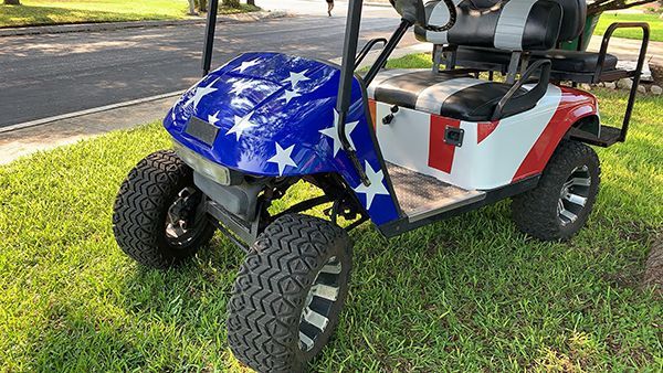 Blue-and-red golf cart on grass, decorated with white stars, beside a road.