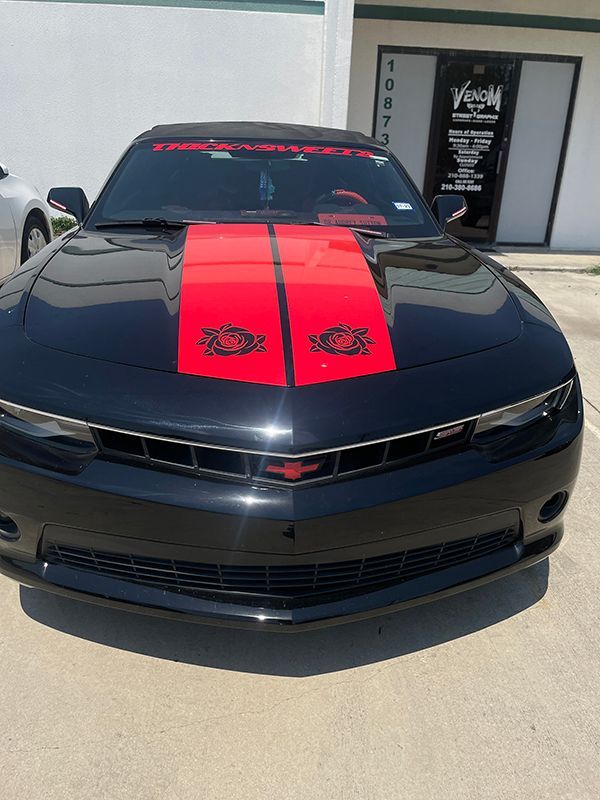 Black Dodge Challenger with red racing stripes parked outside a building