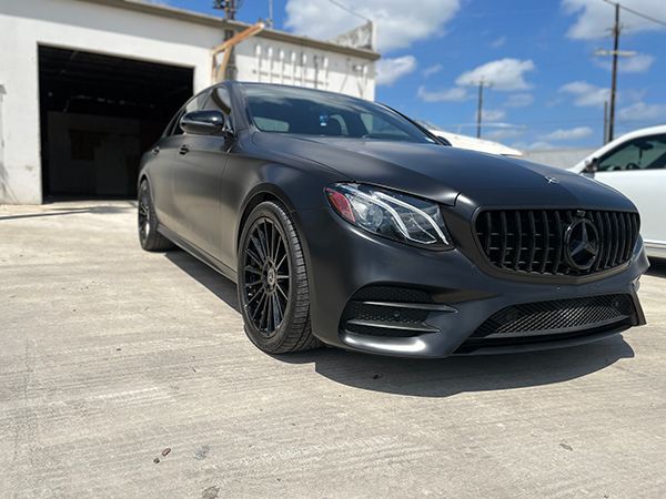Matte black Mercedes coupe parked outside a garage on a sunny day
