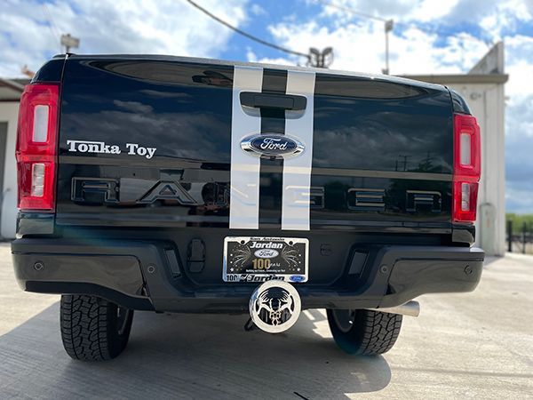 Black Ford pickup with white racing stripe and a tow hitch, parked outdoors under a blue sky