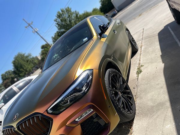 Bronze BMW SUV parked outdoors on a sunny street, angled front view.