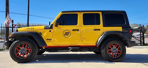Yellow Jeep Wrangler with red-accented wheels parked outdoors in profile view