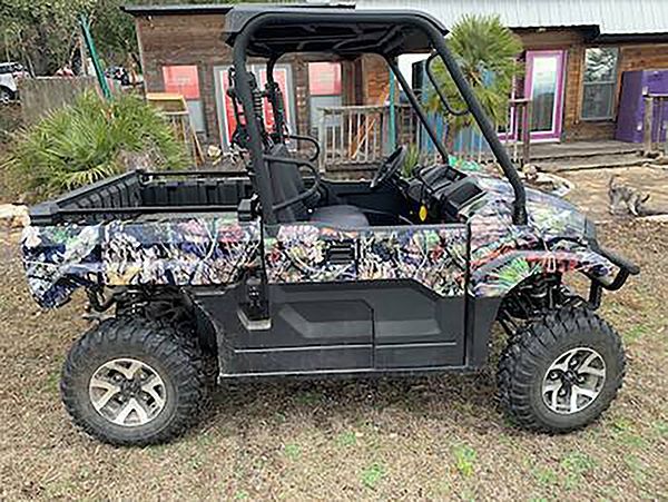 Camouflaged off-road utility vehicle parked in front of a rustic building