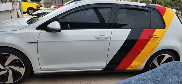 Silver hatchback with black, red, and yellow diagonal stripes on the rear side, parked outdoors.