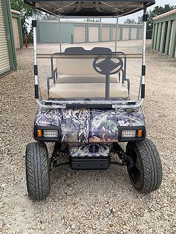 Camouflage golf cart with clear canopy and beige seats parked on gravel