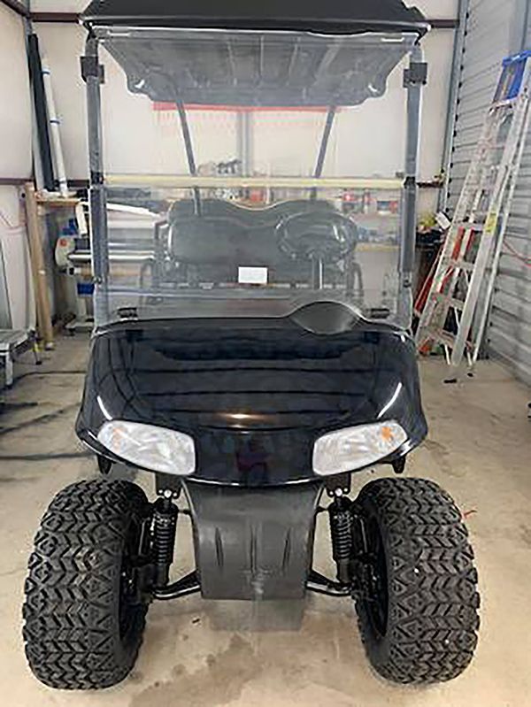 Black golf cart with clear windshield and large off-road tires in a garage.