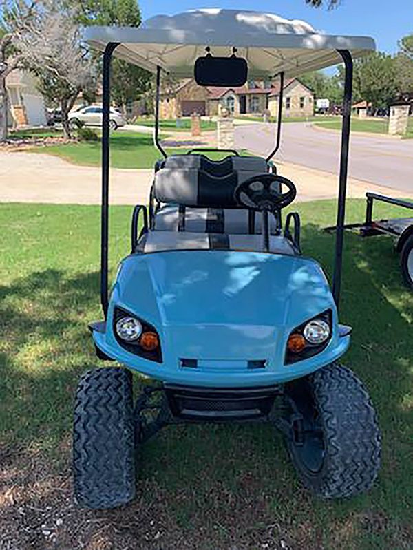 Blue golf cart parked on grass under a canopy in a suburban neighborhood