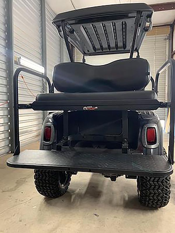 Rear view of a black golf cart with a lifted rear cargo bed inside a garage.