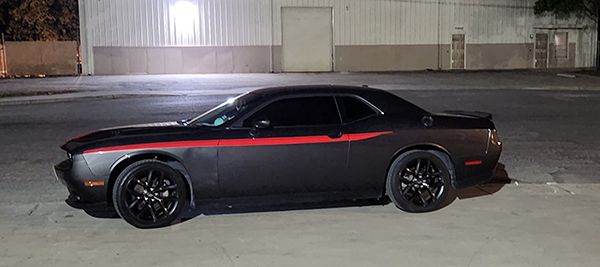 Black sports coupe with a red stripe parked at night in front of a warehouse-like building