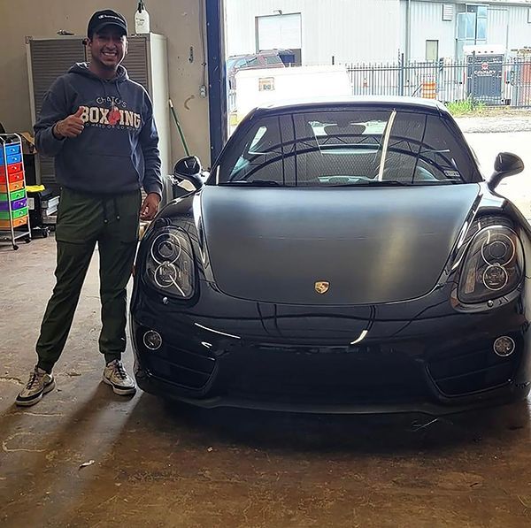 Man standing beside a black Porsche in a garage, smiling and giving a thumbs-up