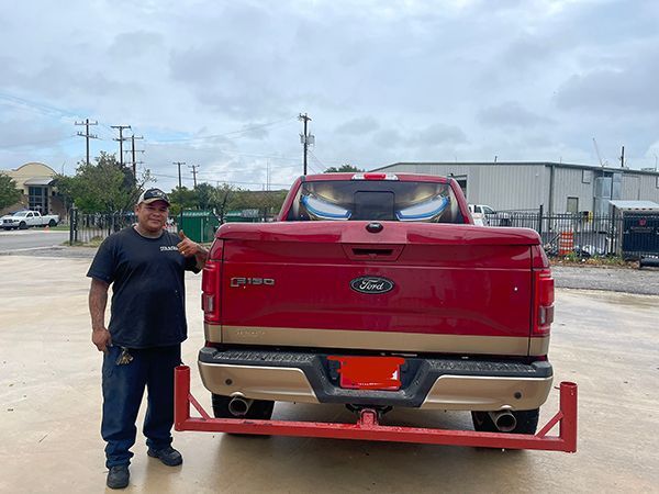 Man standing beside a red Ford pickup with a rear lift attachment in an industrial lot