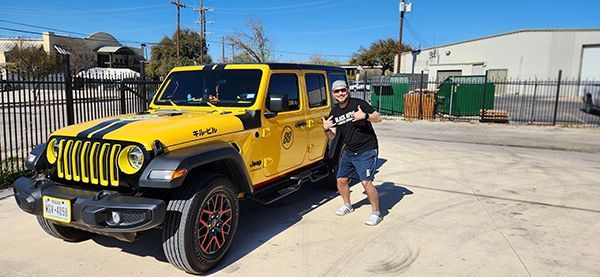 Yellow Jeep Wrangler parked outside an industrial building with a person standing beside it.