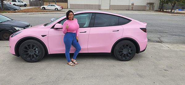 Woman standing beside a pink sedan in a parking lot.