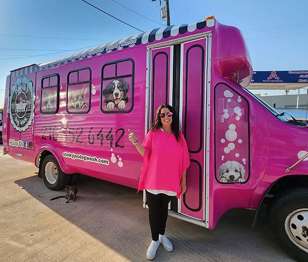 Woman standing beside a bright pink food truck in a sunny parking lot.