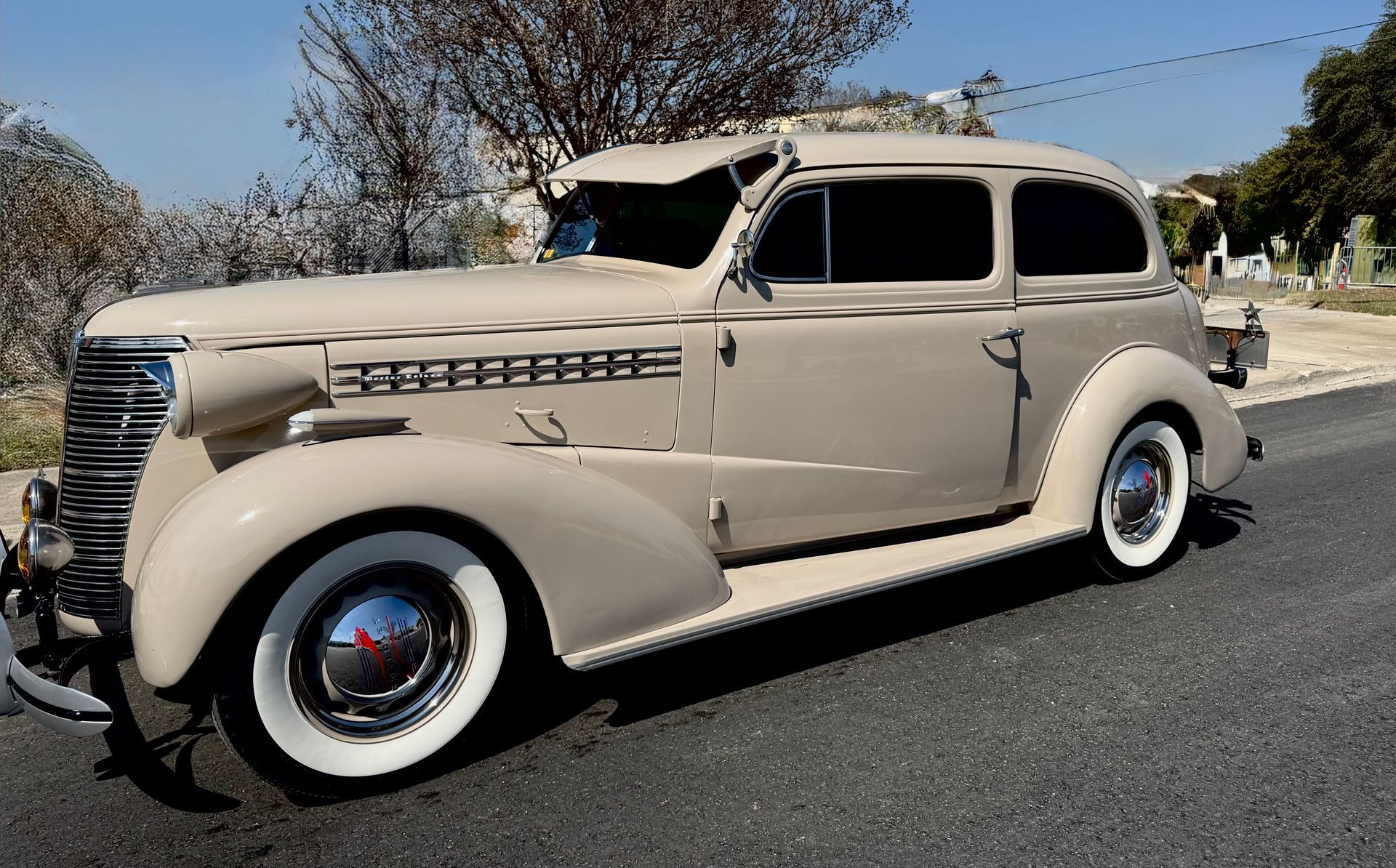 Beige vintage sedan parked on a sunlit street with trees in the background