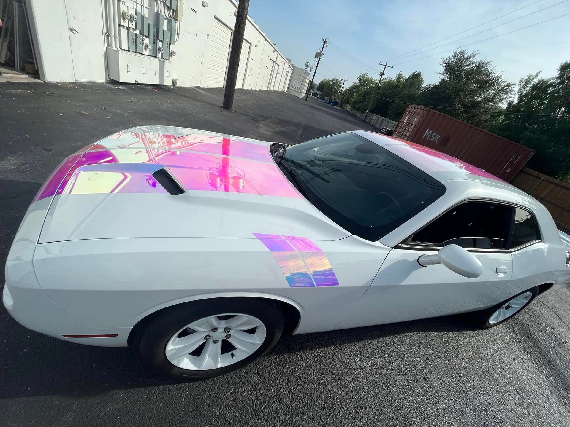 White sports car with pink-and-purple graphics parked beside a building on a street