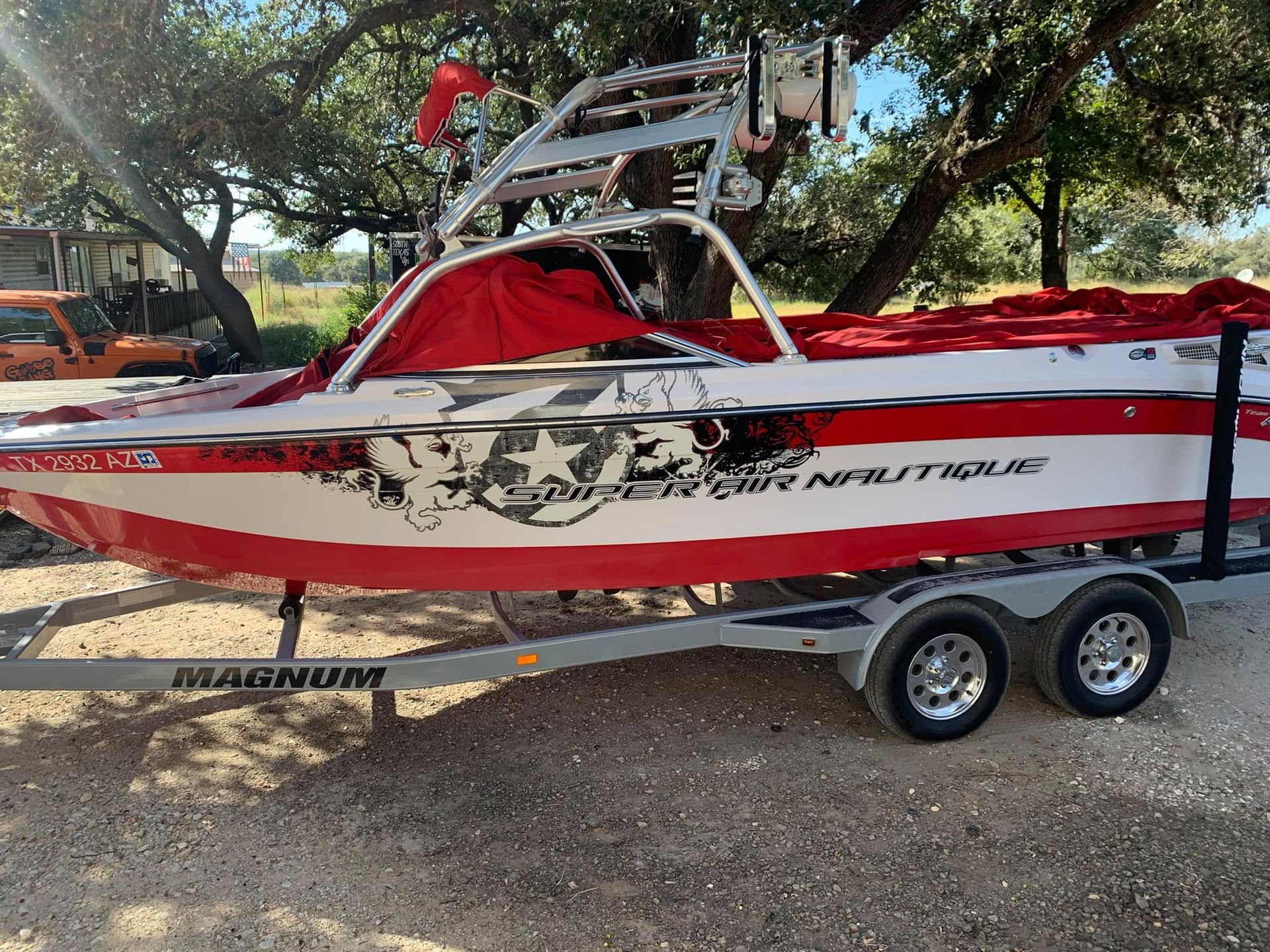 Red and white speedboat on a trailer, parked outdoors under trees.