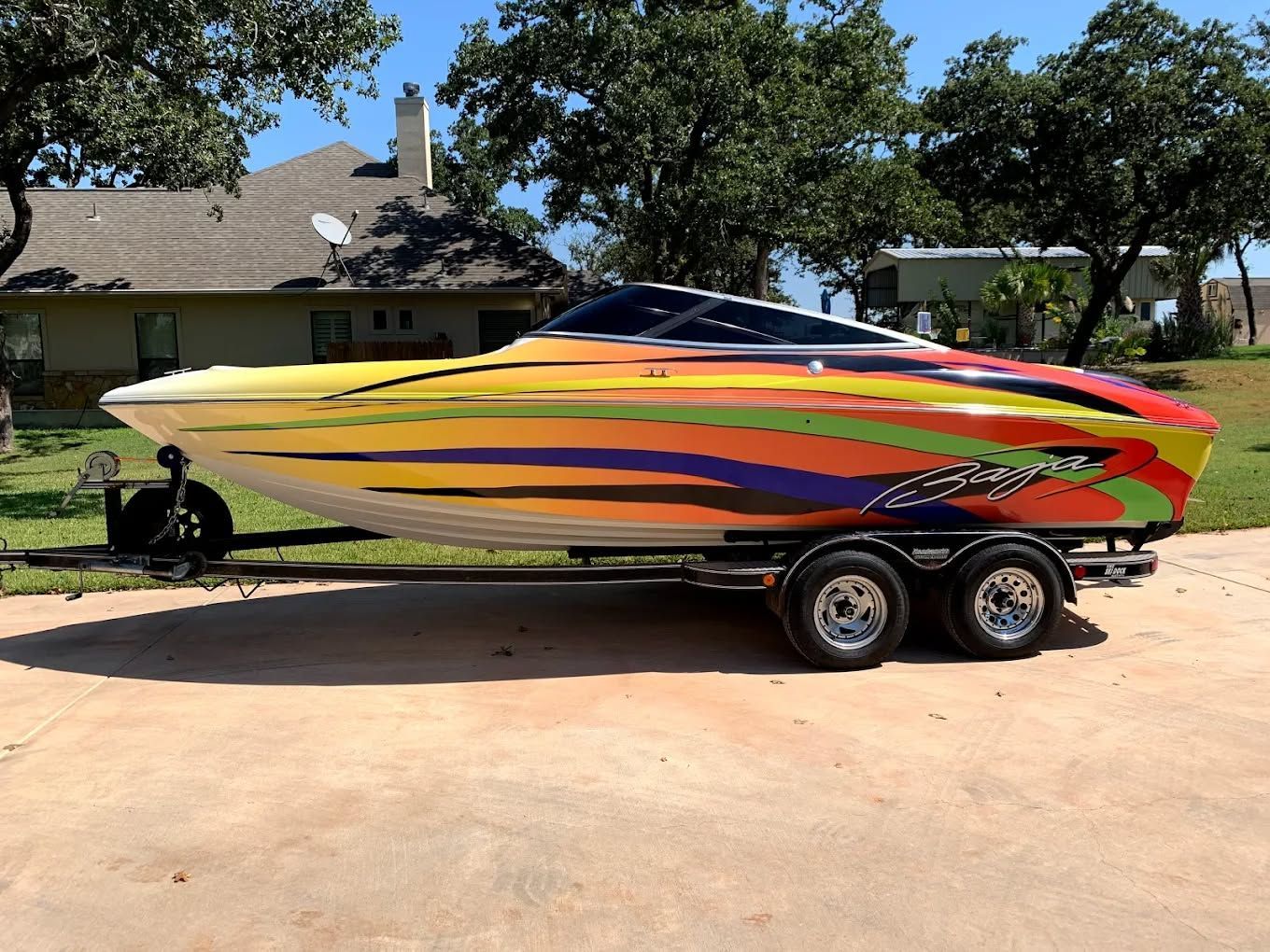 Colorful speedboat on a trailer in a driveway, with trees and a house in the background