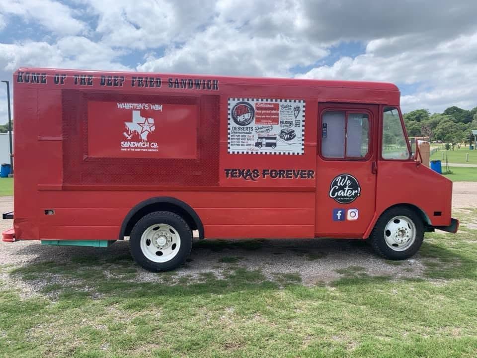 Red food truck parked on grass with awning, menus, and side service window