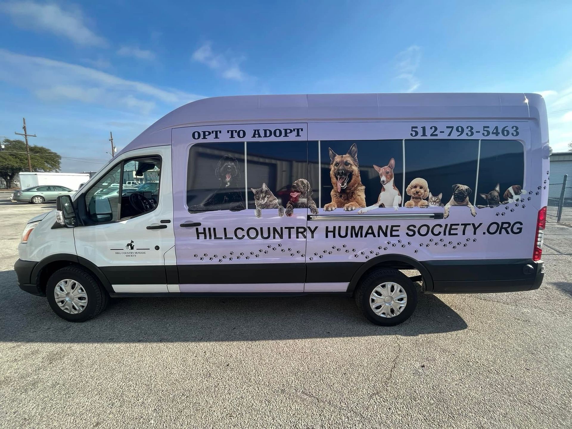 Shelter van with “OP TO ADOPT” and dogs, branded Hill Country Humane Society, parked outdoors