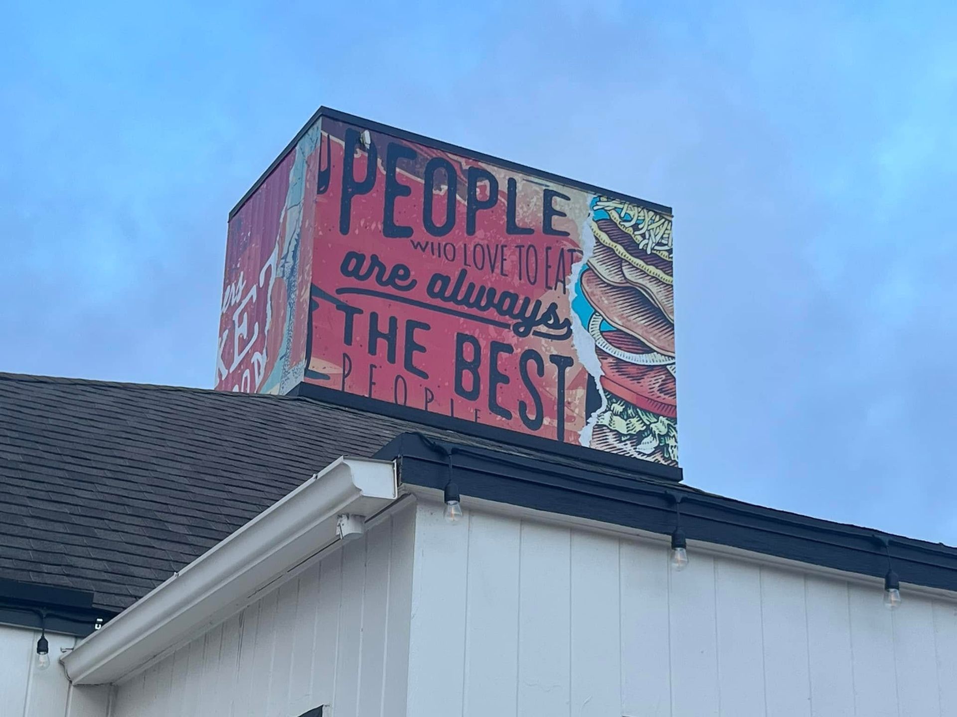 Mural on a rooftop reading “People are always the best” against a blue sky.