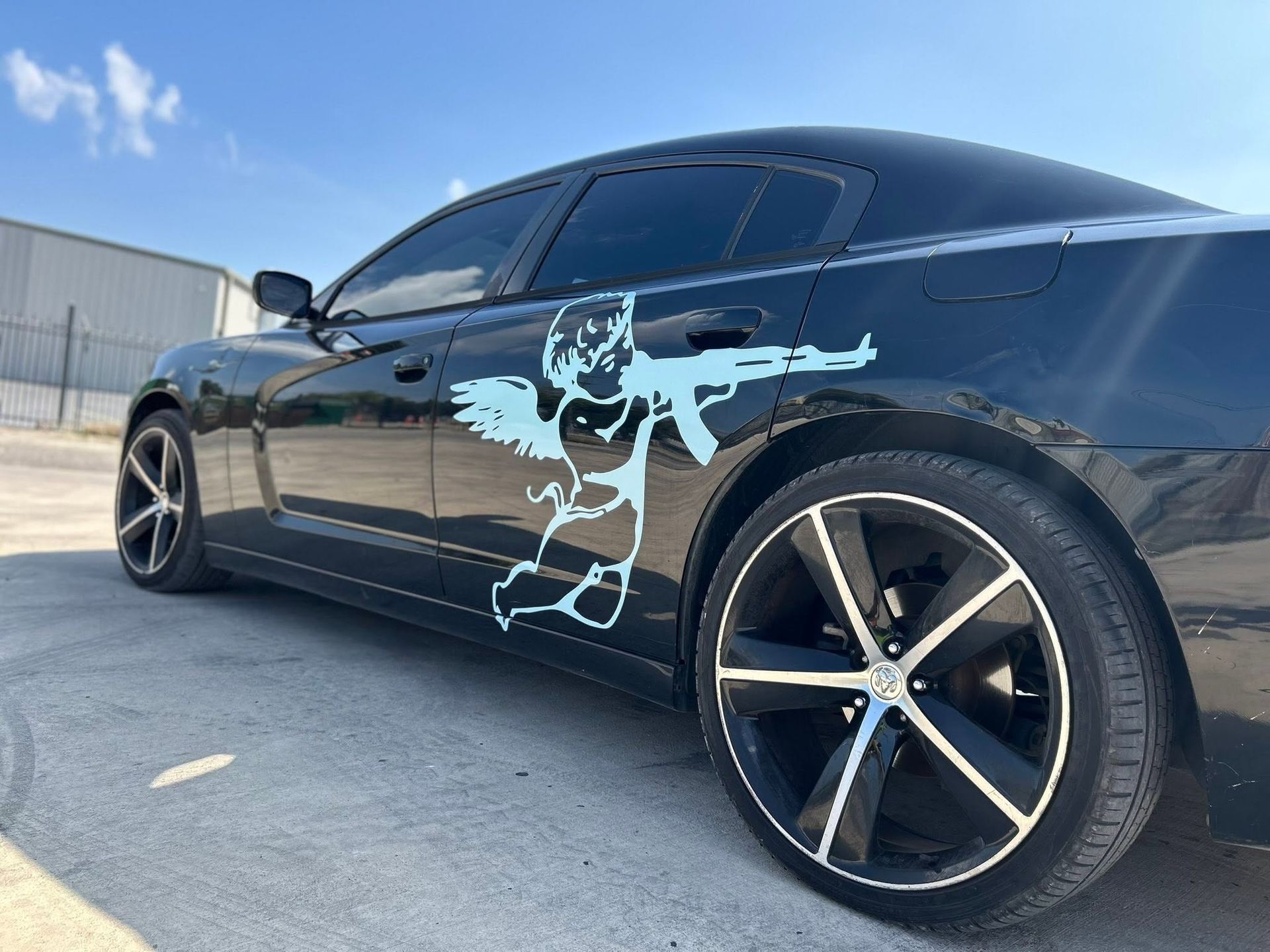 Black sports coupe with a light blue graphic decal, parked on pavement under a clear sky.