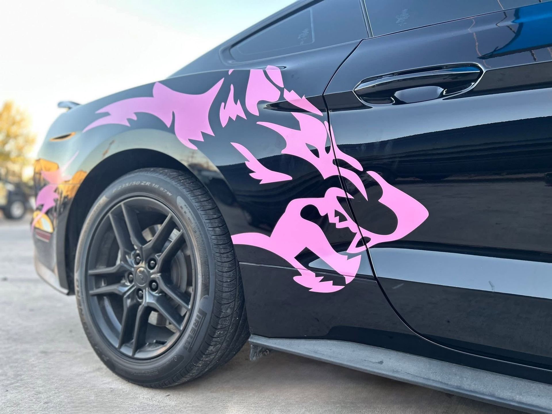 Pink wolf decal on a black car door, parked outdoors.