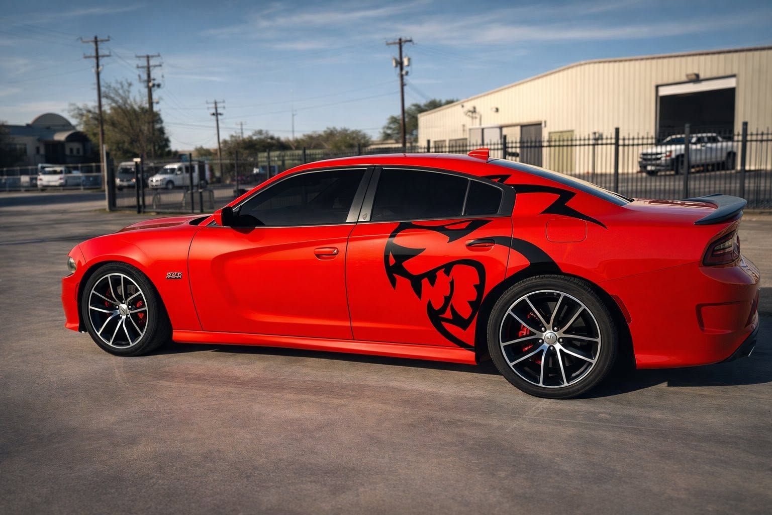Red sports sedan with black graphic parked in an industrial lot under clear sky
