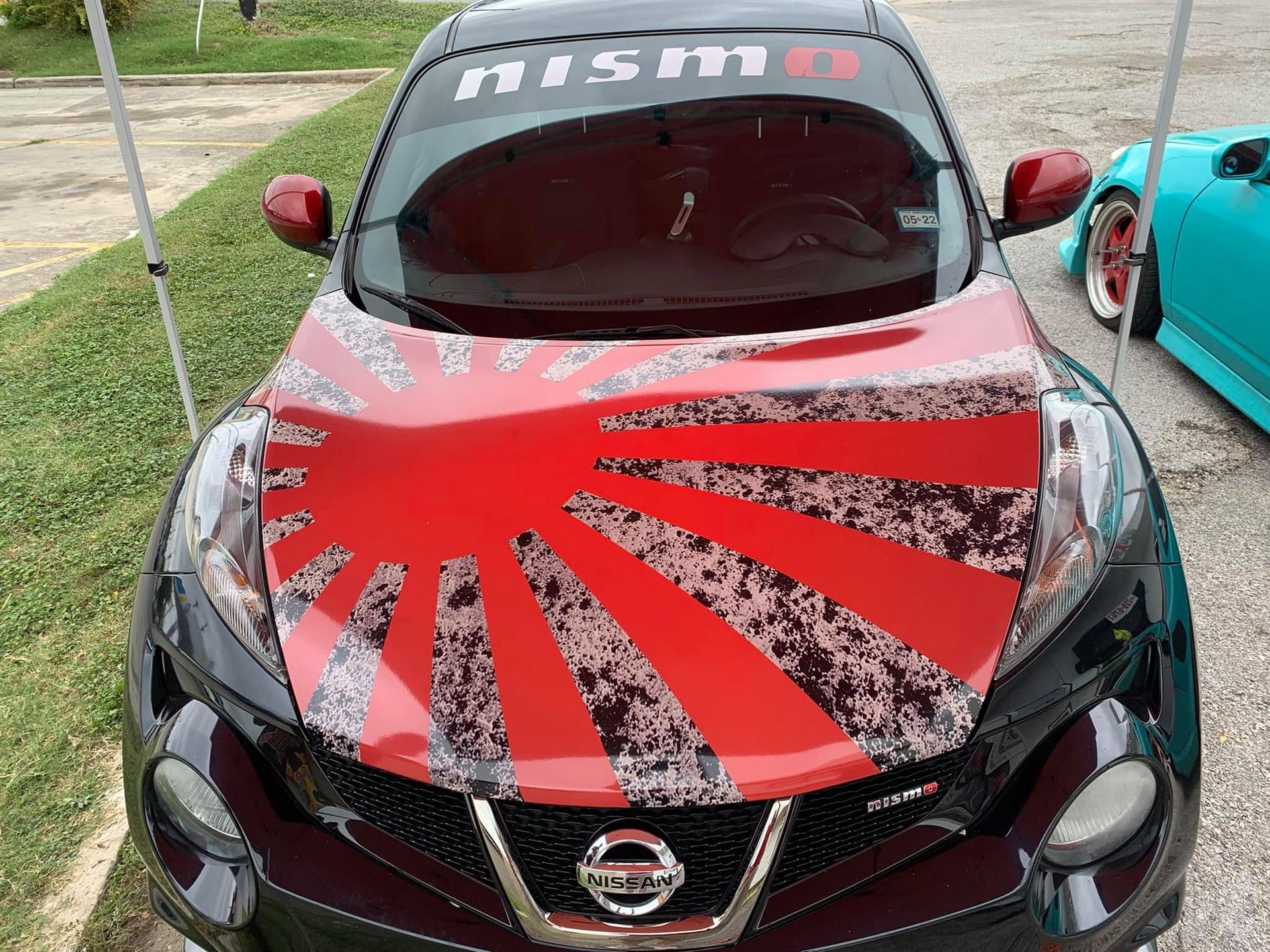 Nissan sports car with red sunburst hood wrap, parked outdoors beside a teal car.