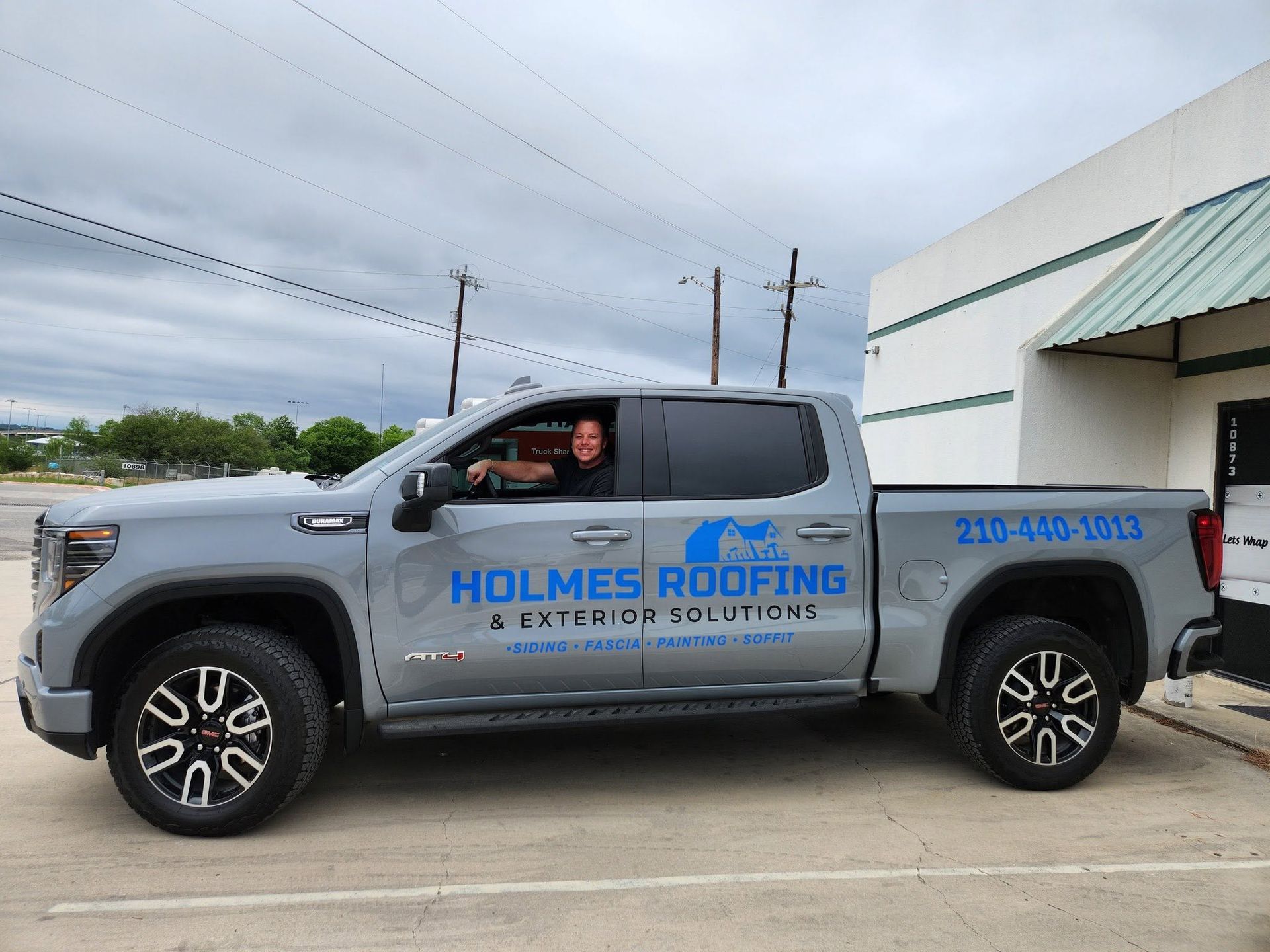 Gray Holmes Roofing pickup truck parked outside a building under cloudy skies