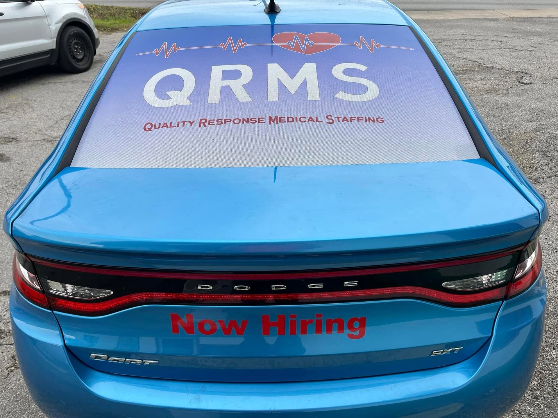 Blue sedan with QRMS branding and “Now Hiring” text on the rear window and trunk lid.