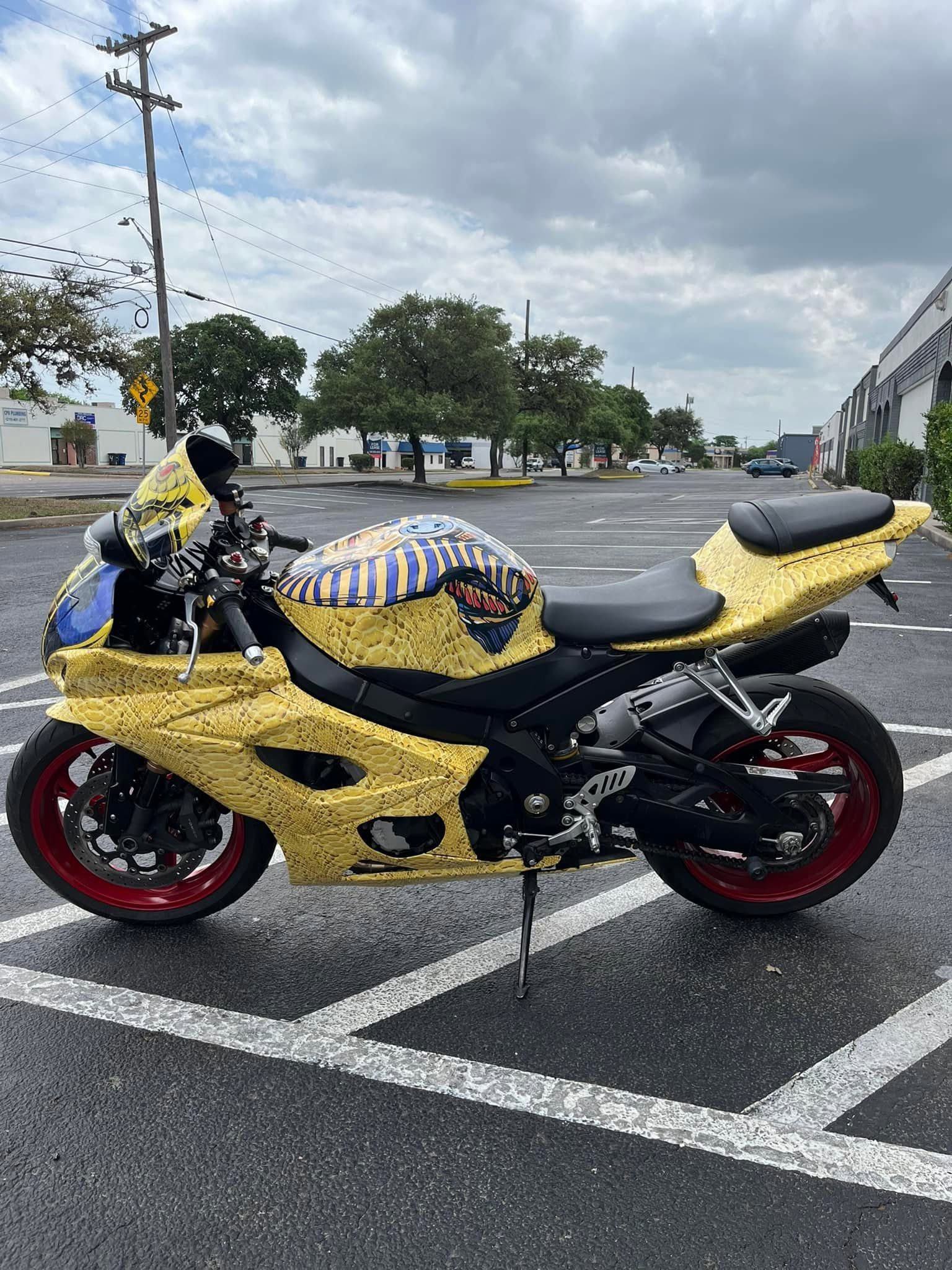 Yellow and black sport motorcycle with red rims parked in an empty lot under cloudy skies