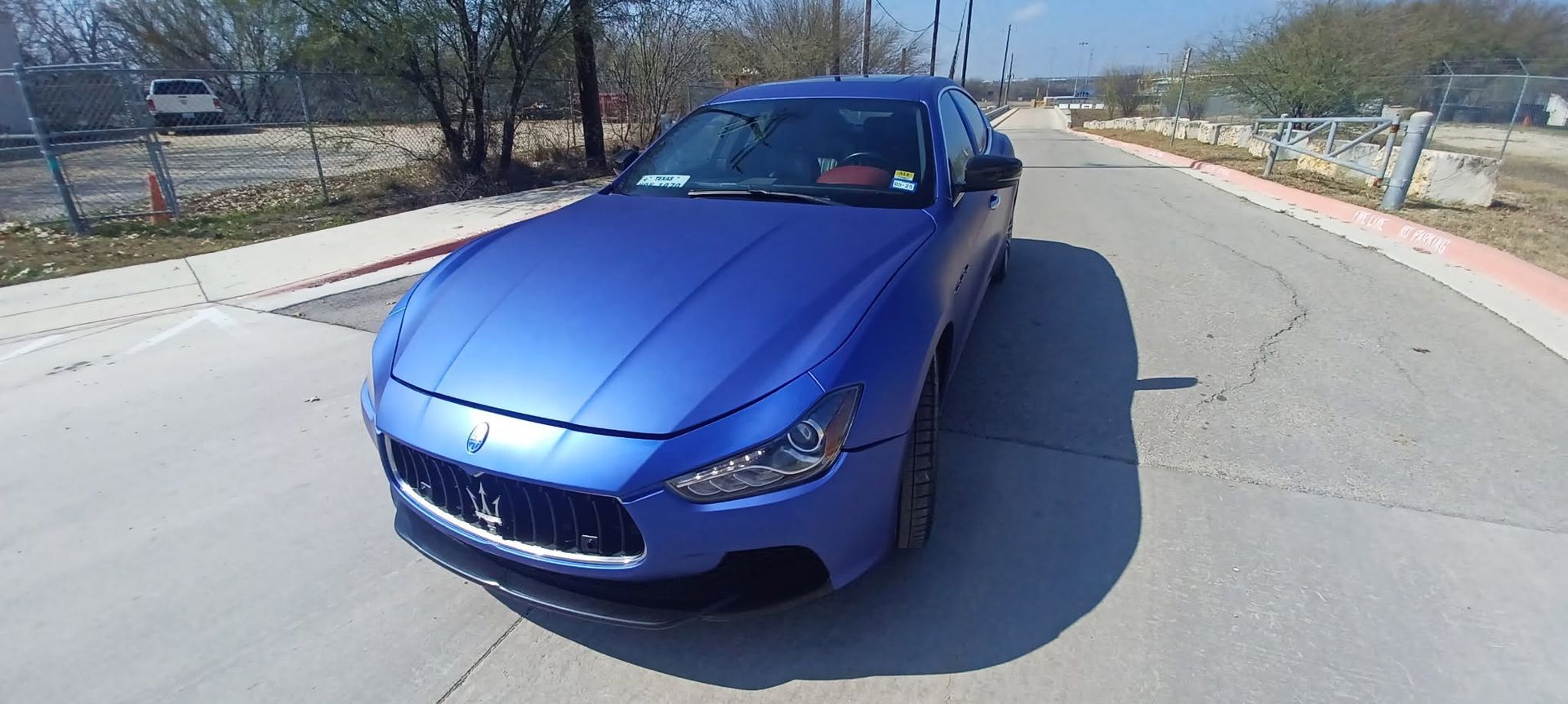 Blue convertible sports car parked on a sunny street corner with a red roof visible through the windshield