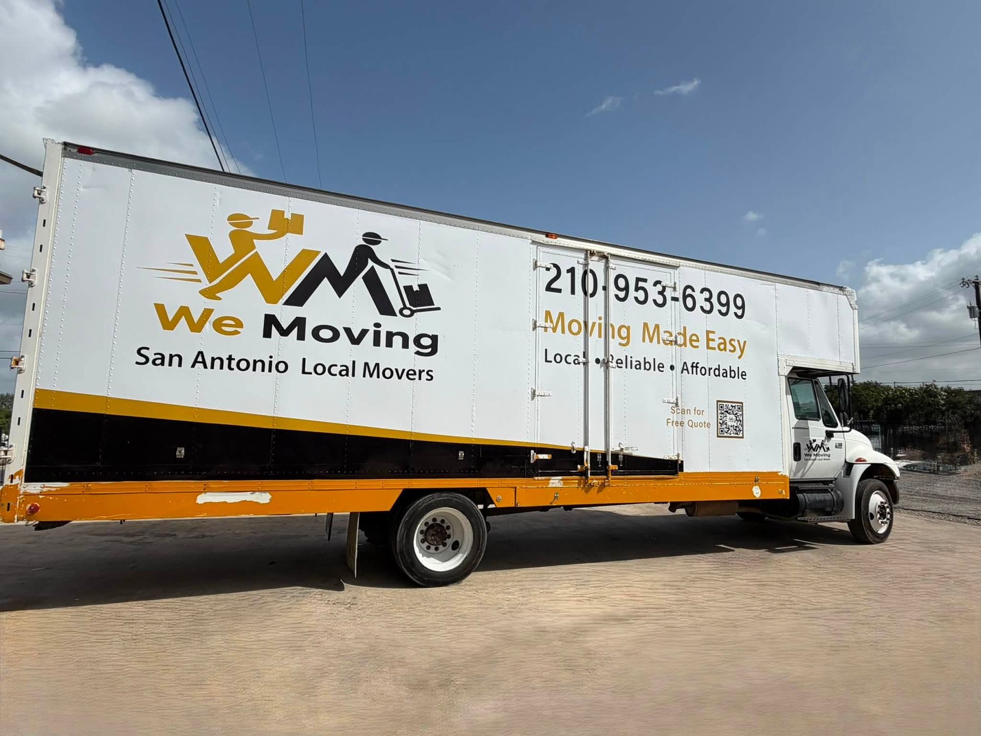 White moving truck with “We Moving” logo parked on a dirt lot under a blue sky