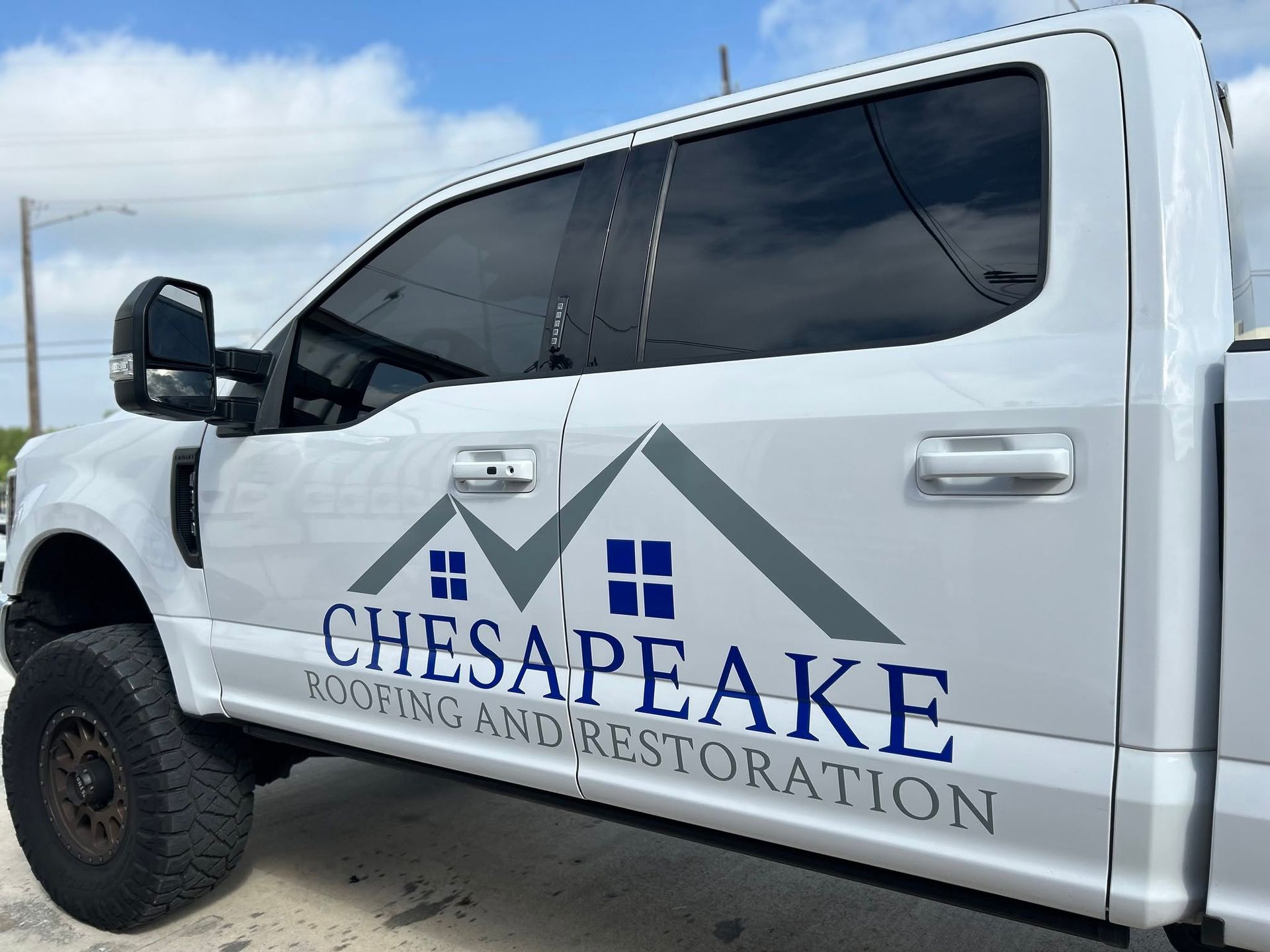 White Chesapeake Moving and Restoration truck with logo and dark tinted windows parked outdoors under a blue sky