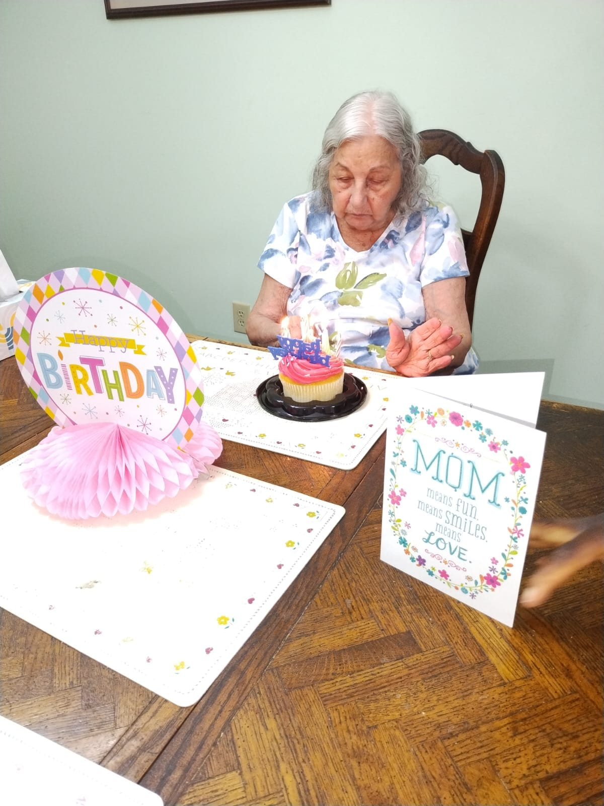 Woman at table with birthday decorations and a cupcake, blowing out candles.