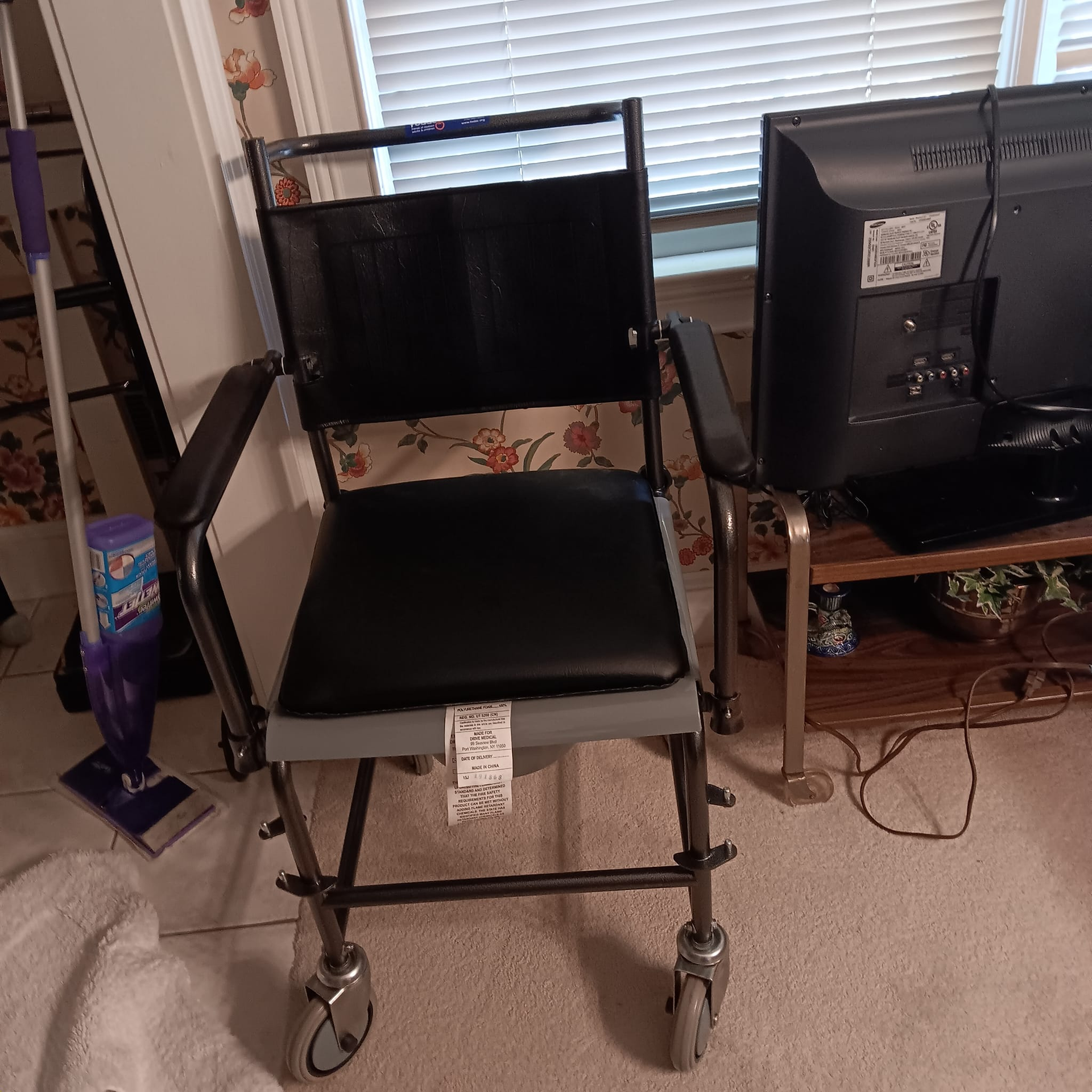 Wheelchair with black seat and back, metal frame, in front of a window and television.
