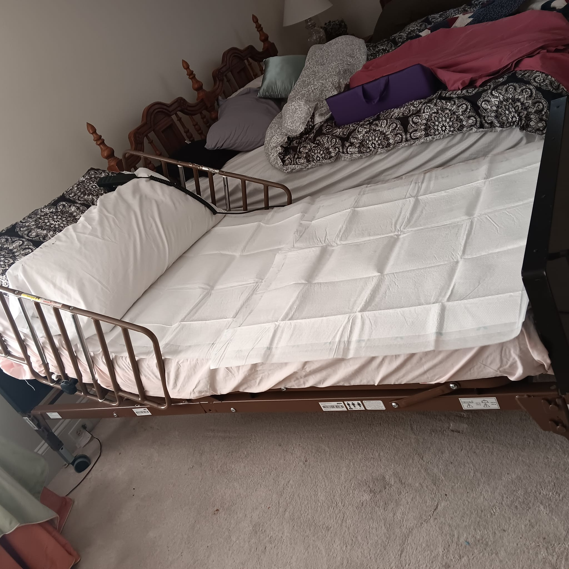 Brown metal hospital bed with safety rails and a white quilted mattress.