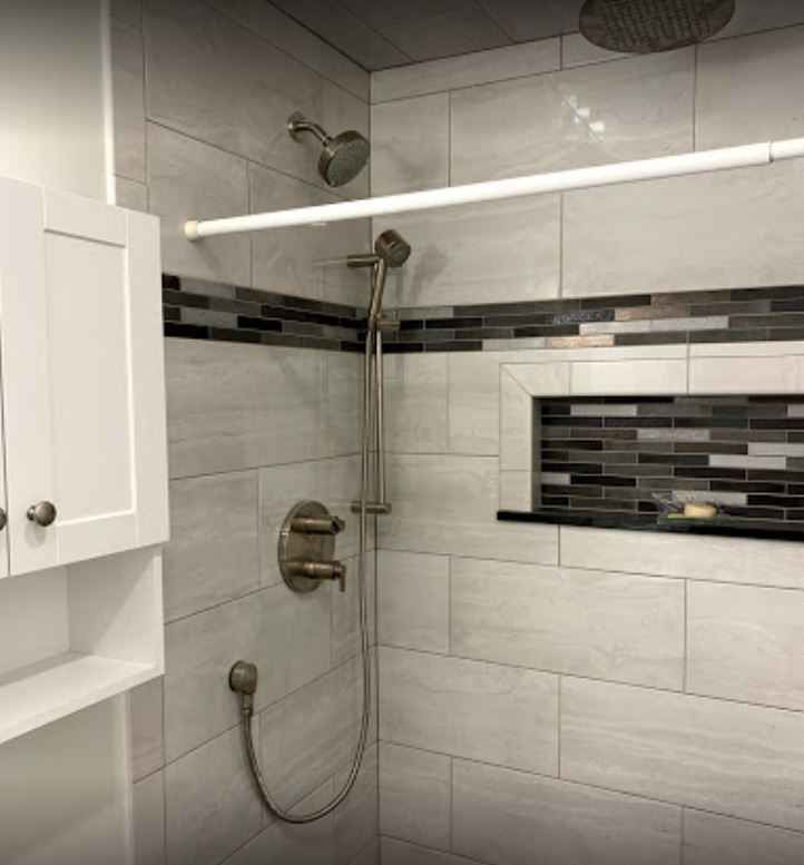 Modern walk-in shower with gray tile, black accent strip, and handheld showerhead