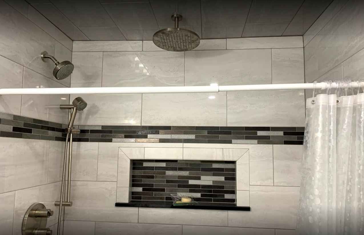 Tiled bathroom shower with chrome fixtures, glass shelf, and black accent tile niche.